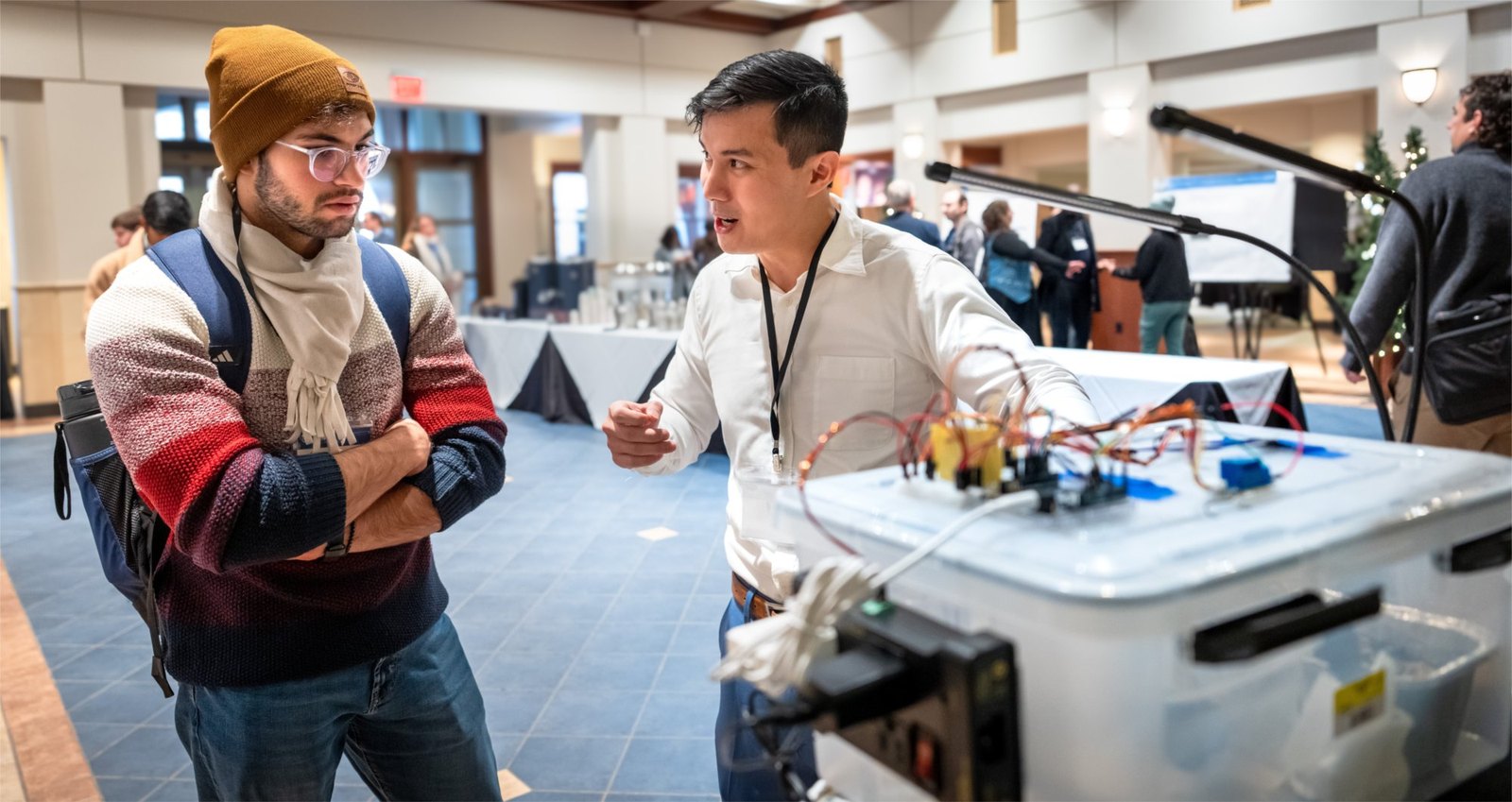 An attendee demonstrating a device with wiring and electronics at a display table